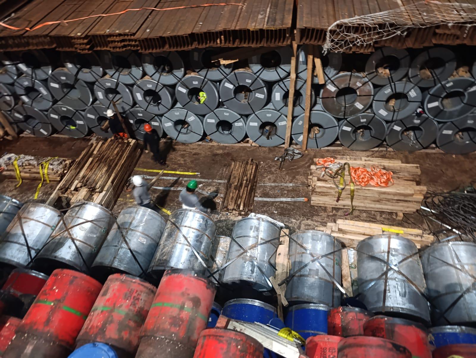 Vista cenital de bobinas de acero estibadas en bodega con cuadrilla trabajando