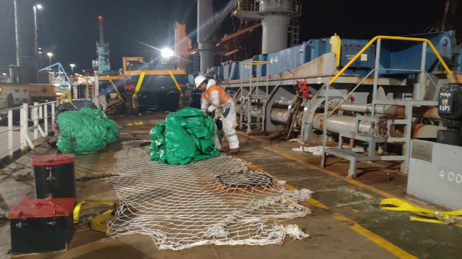 Estibadores retirando eslingas sobre carga cubierta con lonas rojas dentro de la bodega