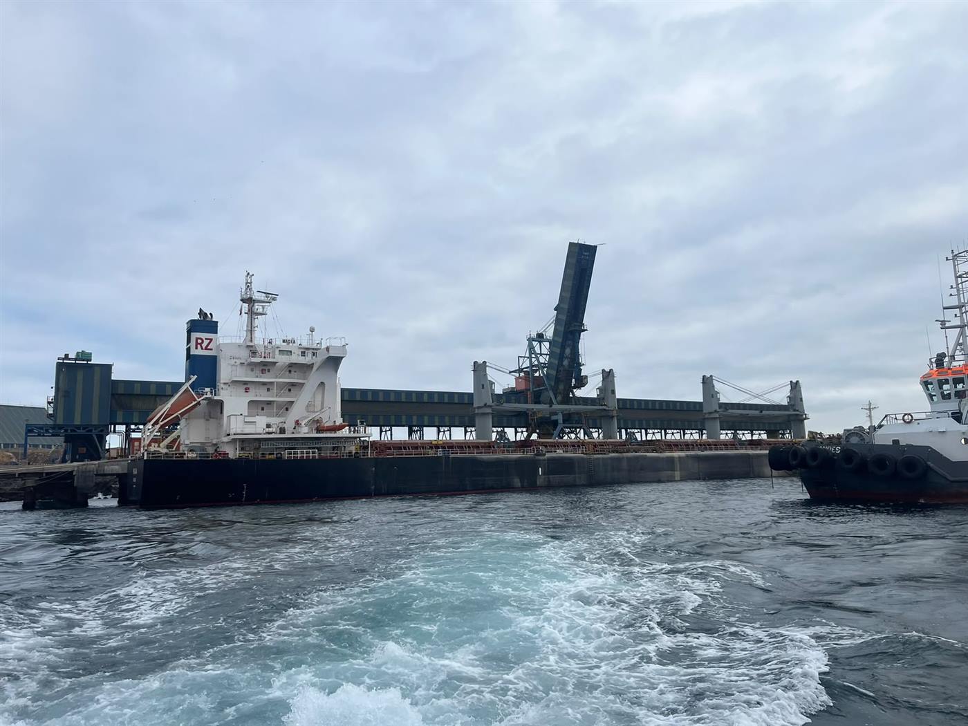 Granelero atracado en terminal de graneles, con remolcador en primer plano